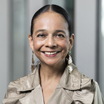 A woman in a gray collared shirt stands and smiles