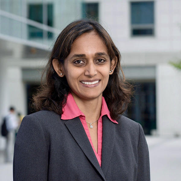 A woman in a gray suit and a pink collared shirt stands and smiles