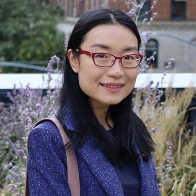 A woman in a blue jacket stands outside and smiles