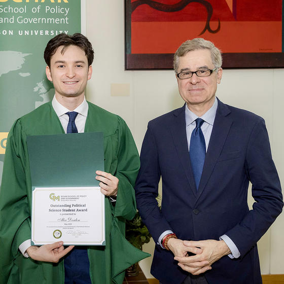 A man in a green gown stands next to a man in a blue suit.