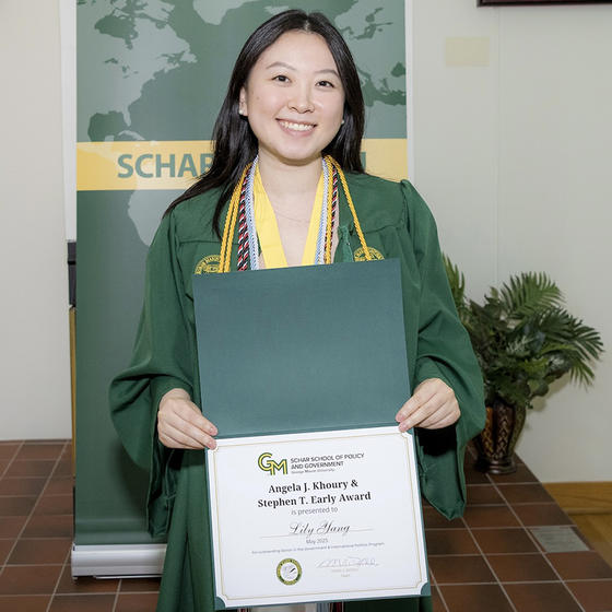 A woman in a green gown holds a certificate and smiles.